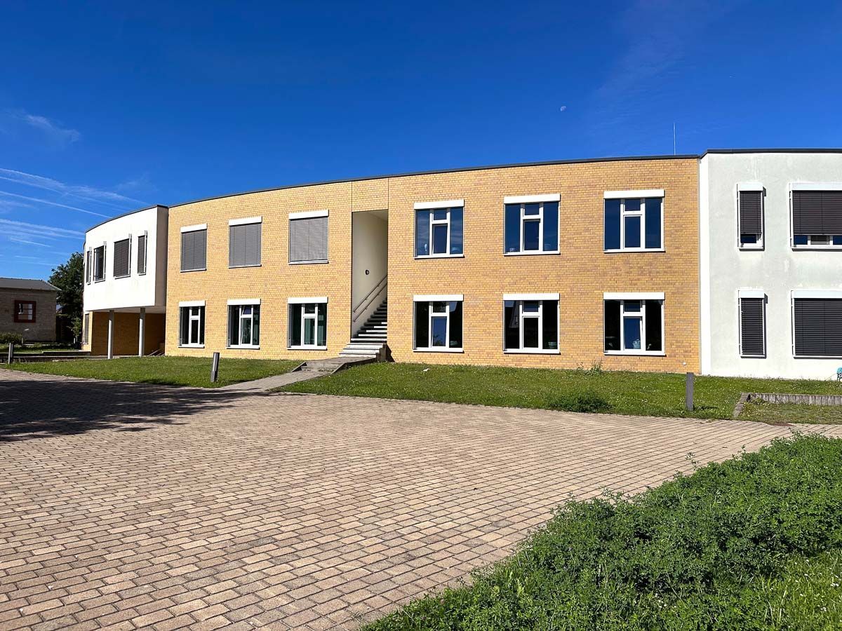 ein großes Backsteingebäude mit vielen Fenstern und einem gepflasterten Gehweg davor - Referenzen von BAUSON GmbH aus Gräfenhainichen