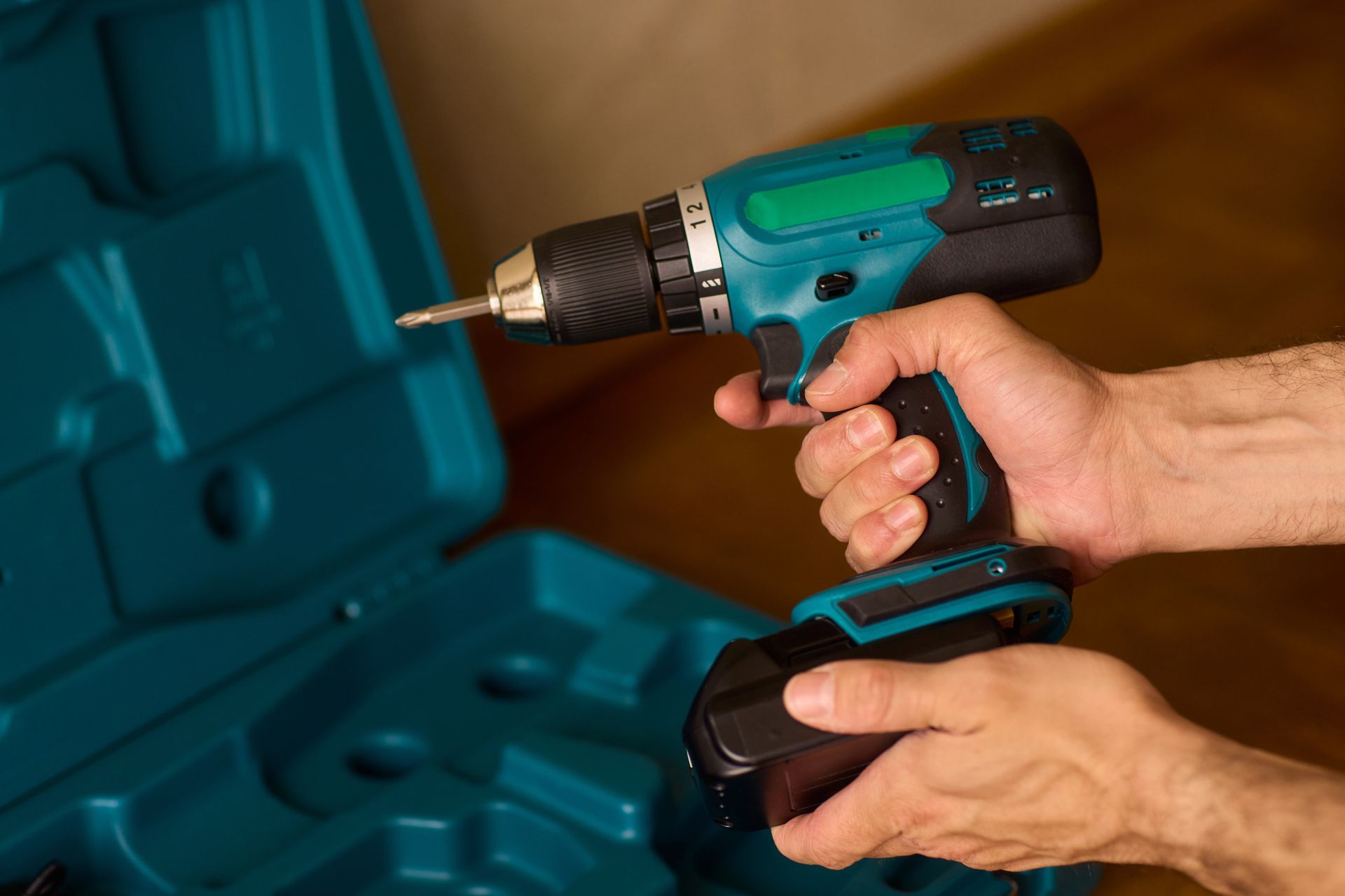Personne tenant une perceuse sans fil turquoise et noir, prête à l'utiliser.