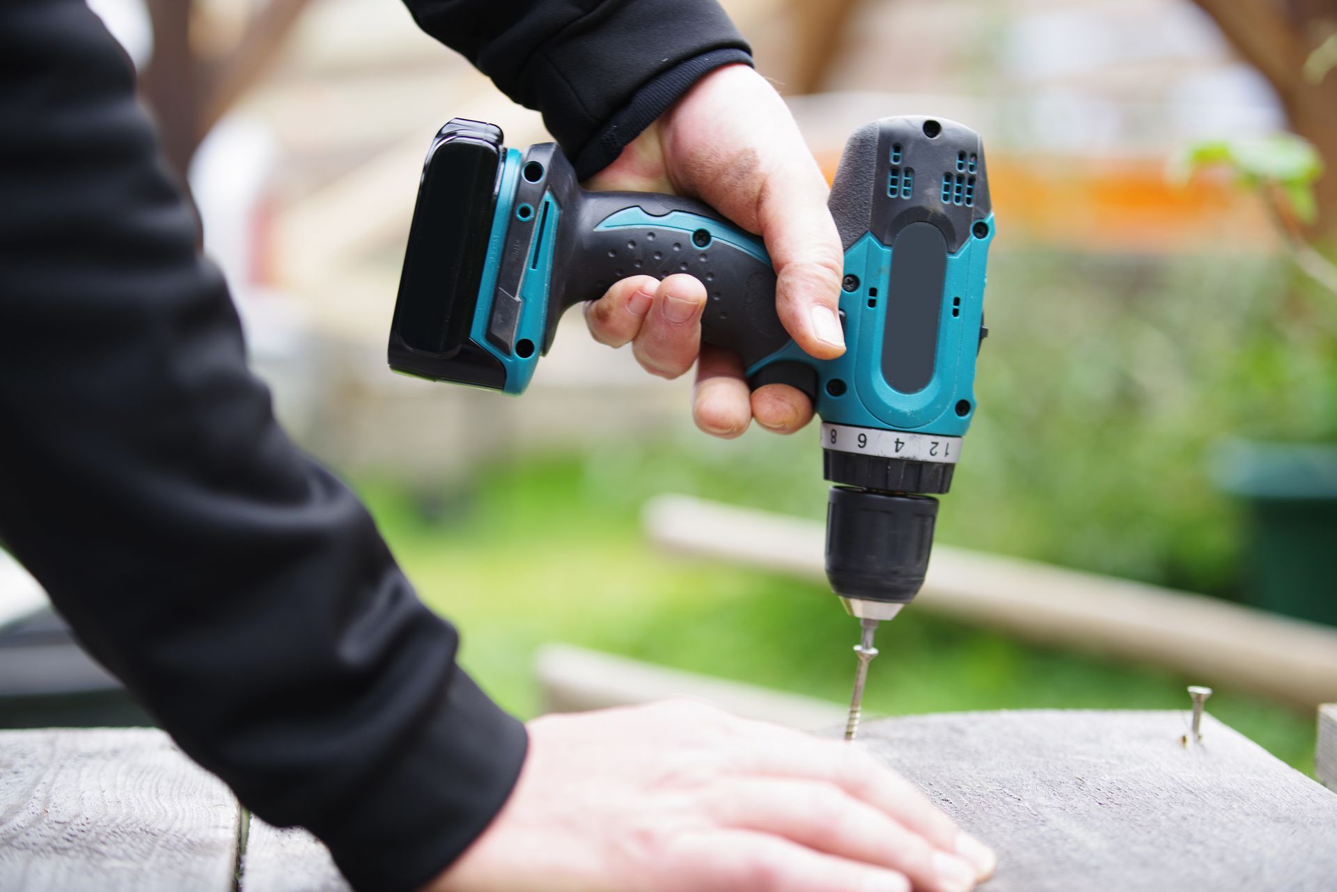 Personne utilisant une perceuse sans fil turquoise et noire pour visser une vis dans une surface en bois.