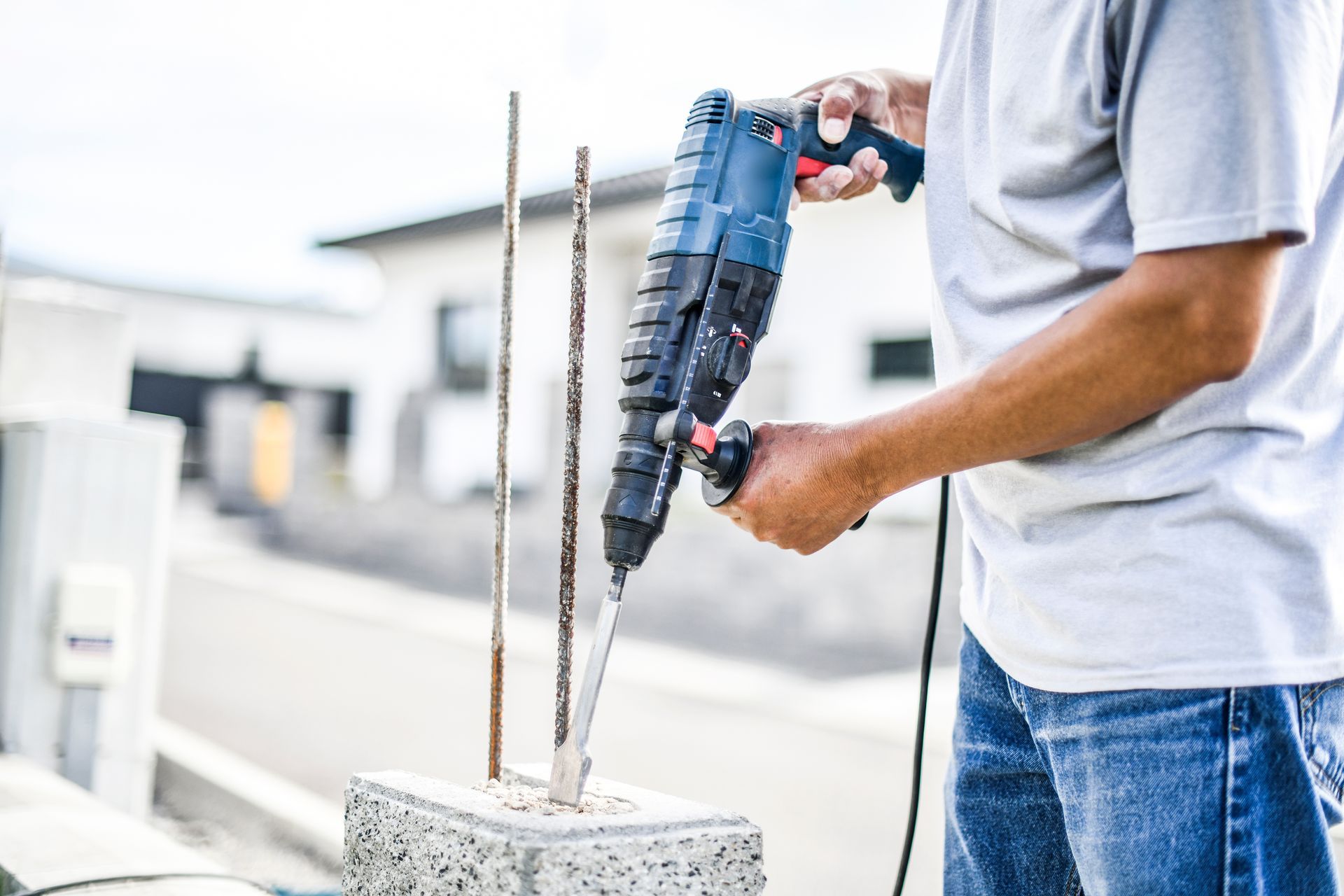 Une personne utilise une perceuse bleue pour travailler sur du béton en extérieur.