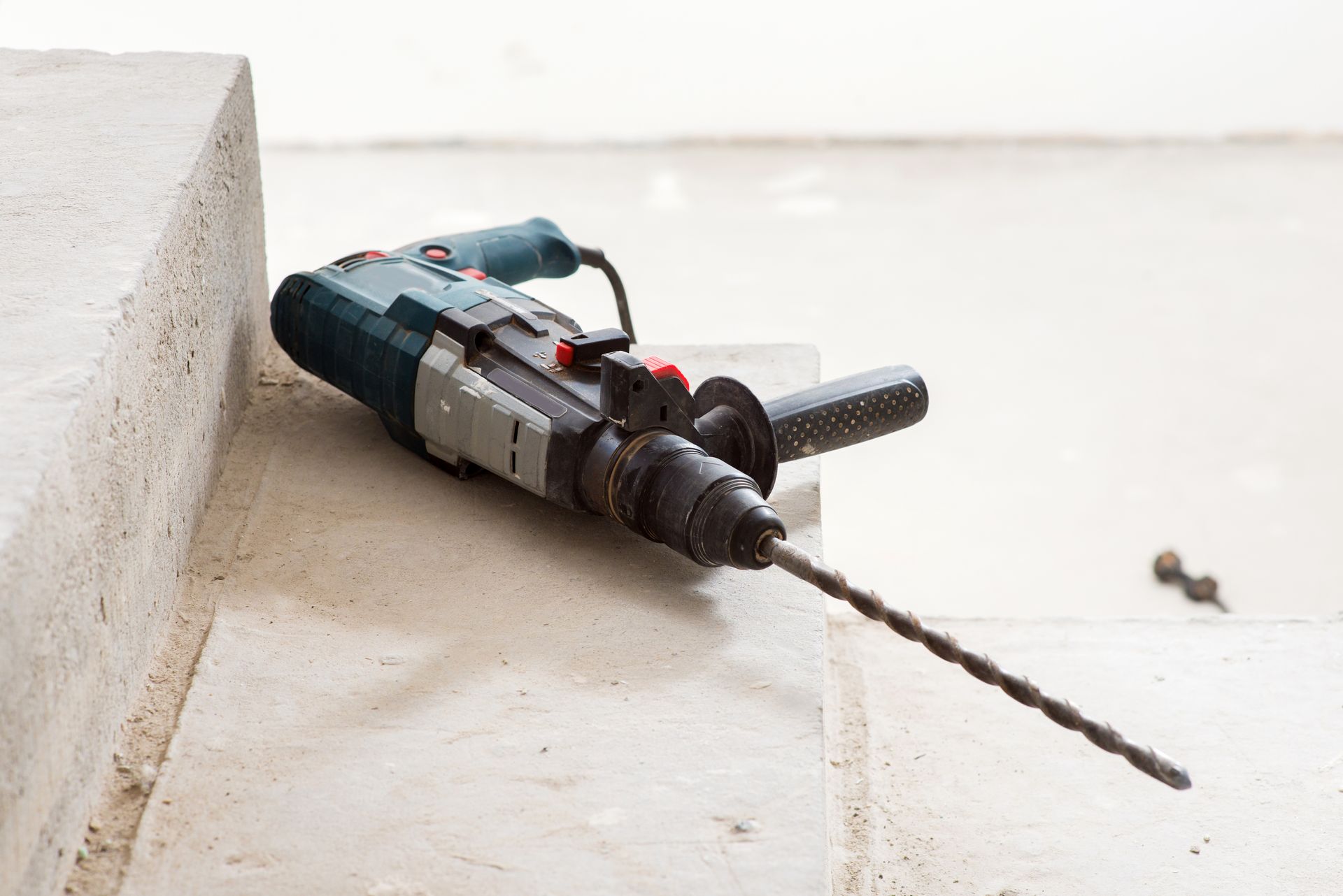 Une perceuse électrique avec un long foret repose sur des marches en béton.