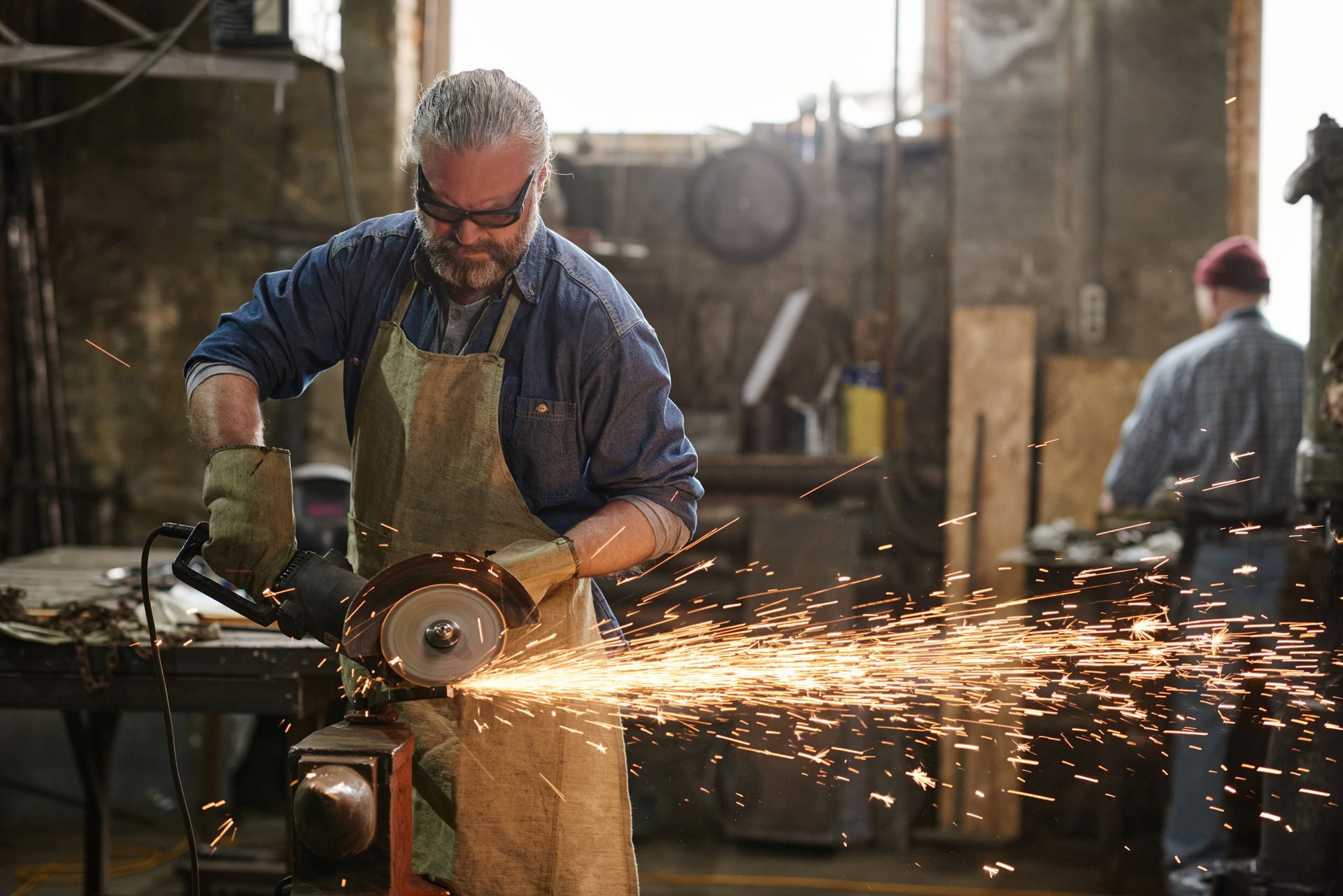 Un homme utilise une meuleuse dans un atelier, des étincelles jaillissent.