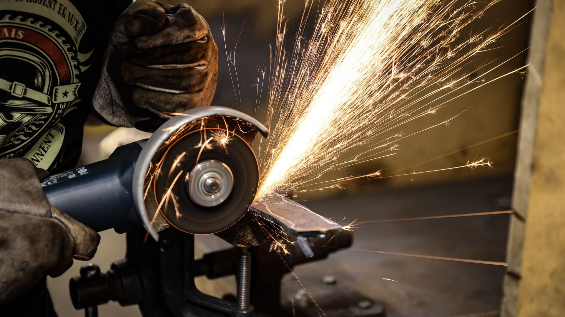 Une personne portant des gants, meulant du métal avec un outil électrique, produisant des étincelles.