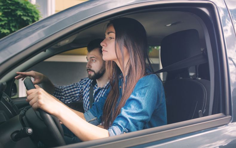 Deux personnes dans une voiture, l'une au volant et l'autre assise côté passager, toutes deux concentrées sur la route.
