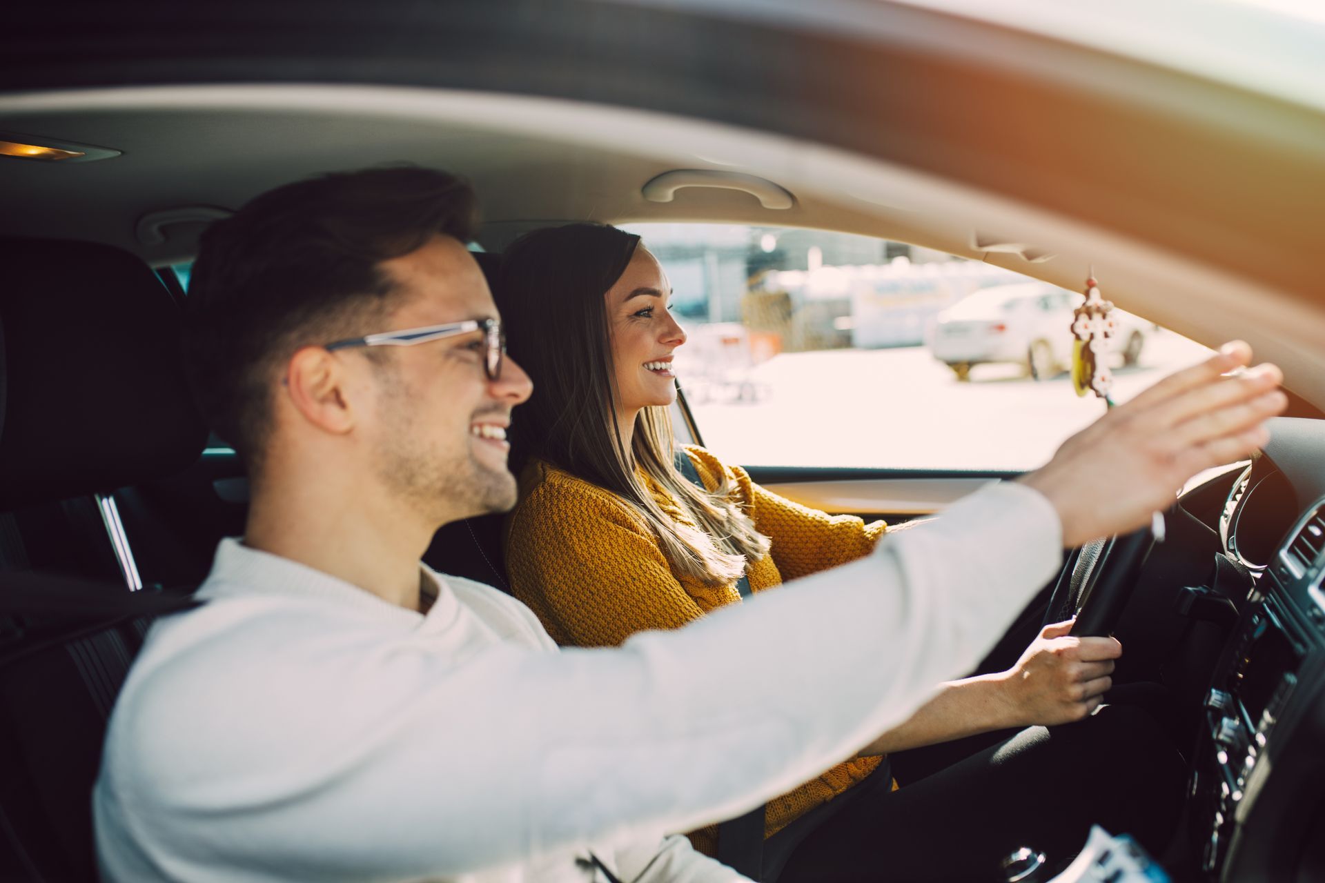 Deux personnes sourient dans une voiture, l'une au volant et l'autre sur le siège passager.