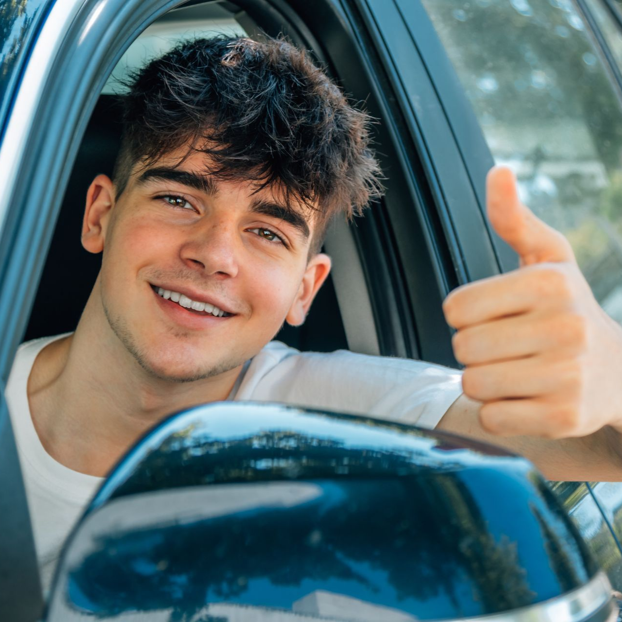 Un conducteur souriant fait un signe de pouce levé depuis la fenêtre de sa voiture.