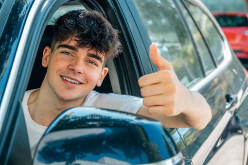 Un garçon souriant dans une voiture fait un signe de pouce levé par la fenêtre ouverte.