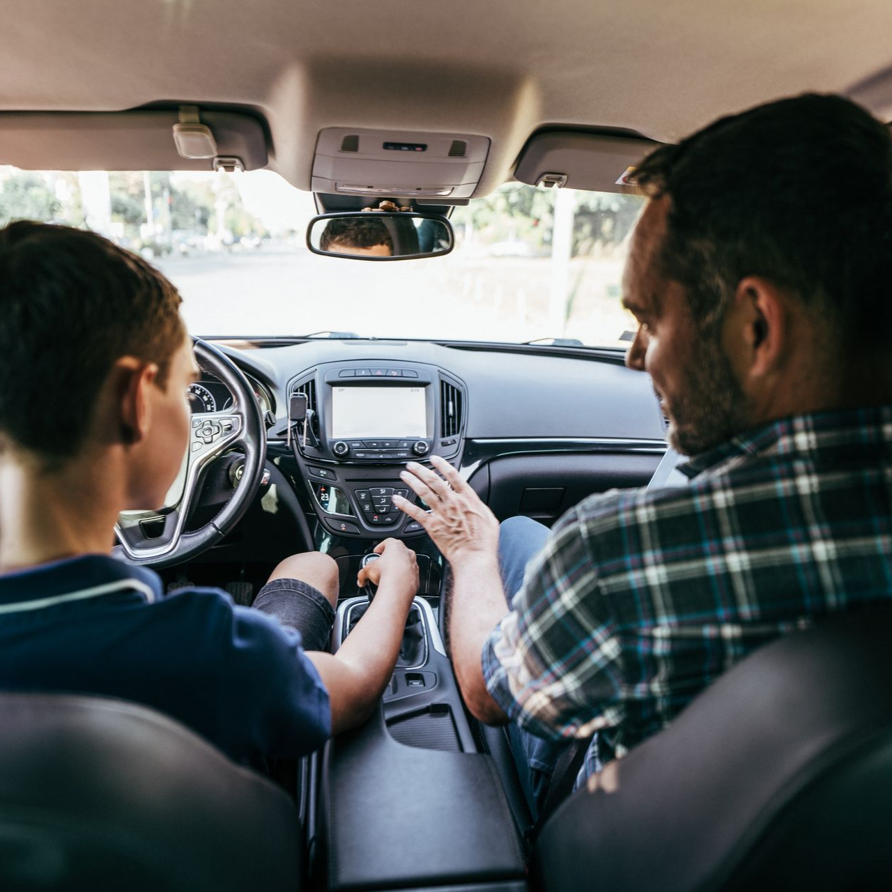Deux personnes dans une voiture, l'une apprenant à l'autre à conduire, les mains sur la console centrale et le volant.