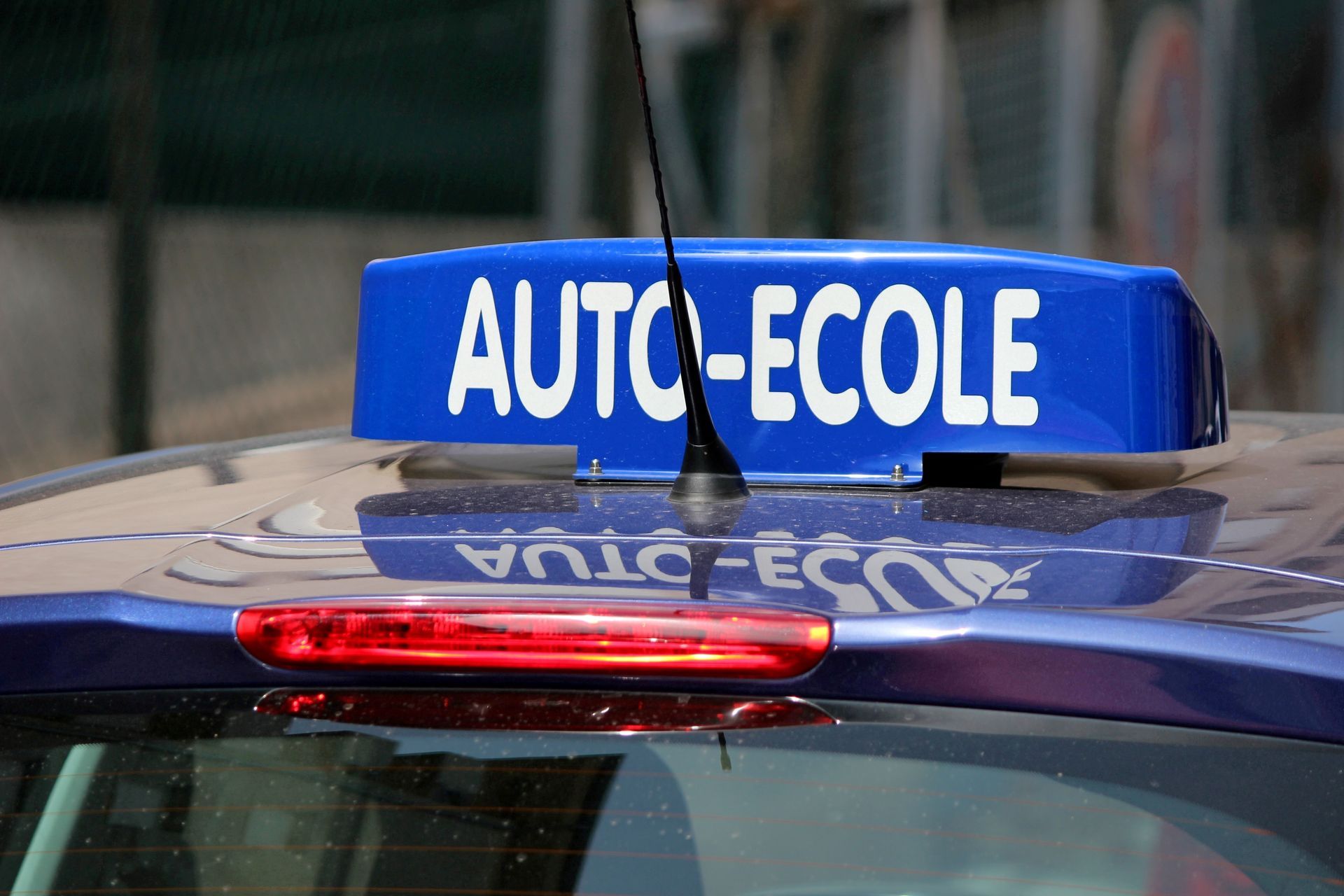 Gros plan d'un panneau bleu AUTO-ÉCOLE sur le toit d'une voiture.