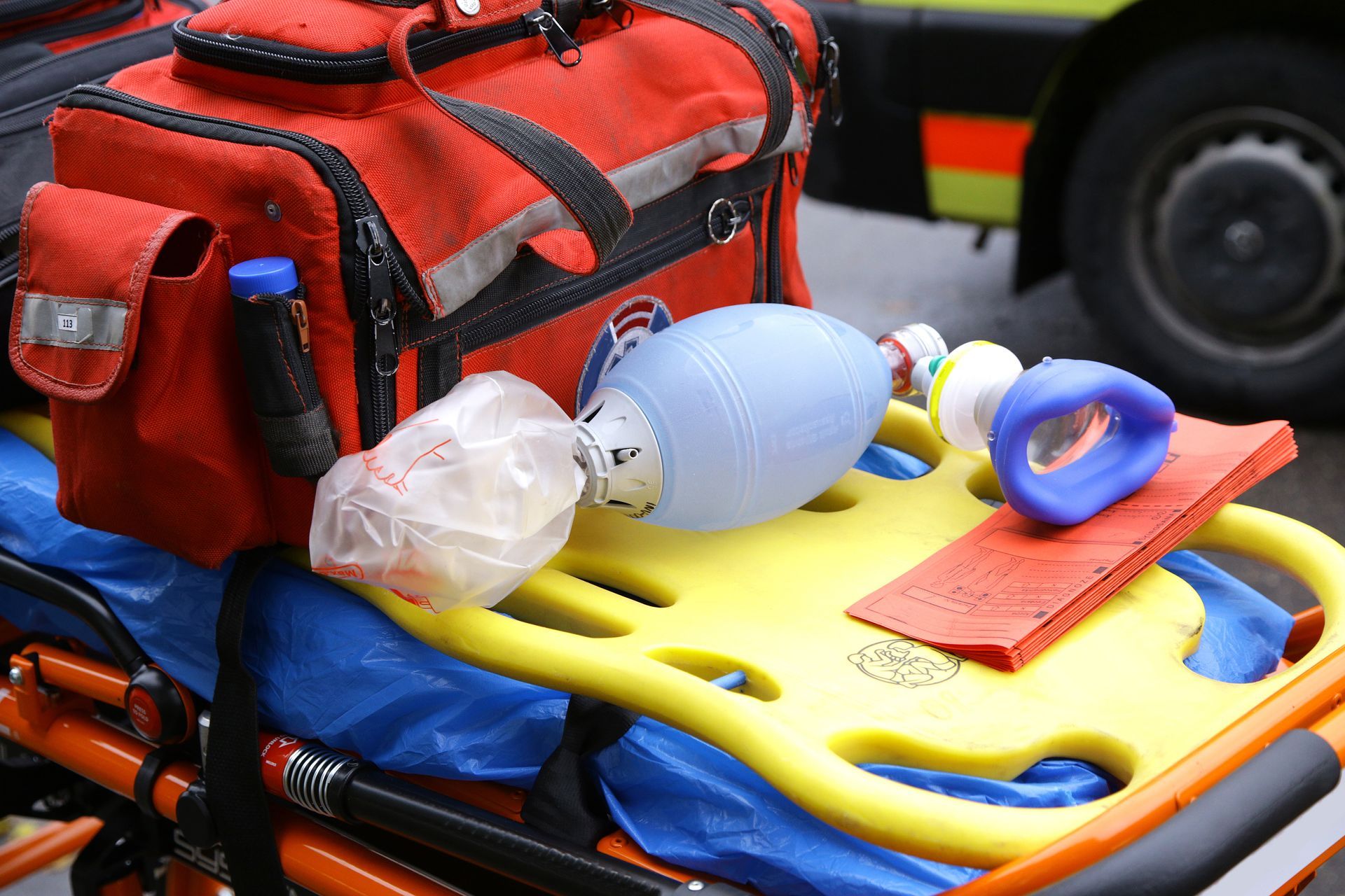 Sac d'urgence rouge contenant du matériel médical sur une civière, comprenant un masque, un flacon, des gants et une pochette rouge