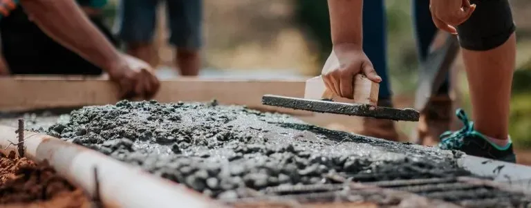 Primer plano de unas manos que utilizan una llana para alisar el hormigón fresco