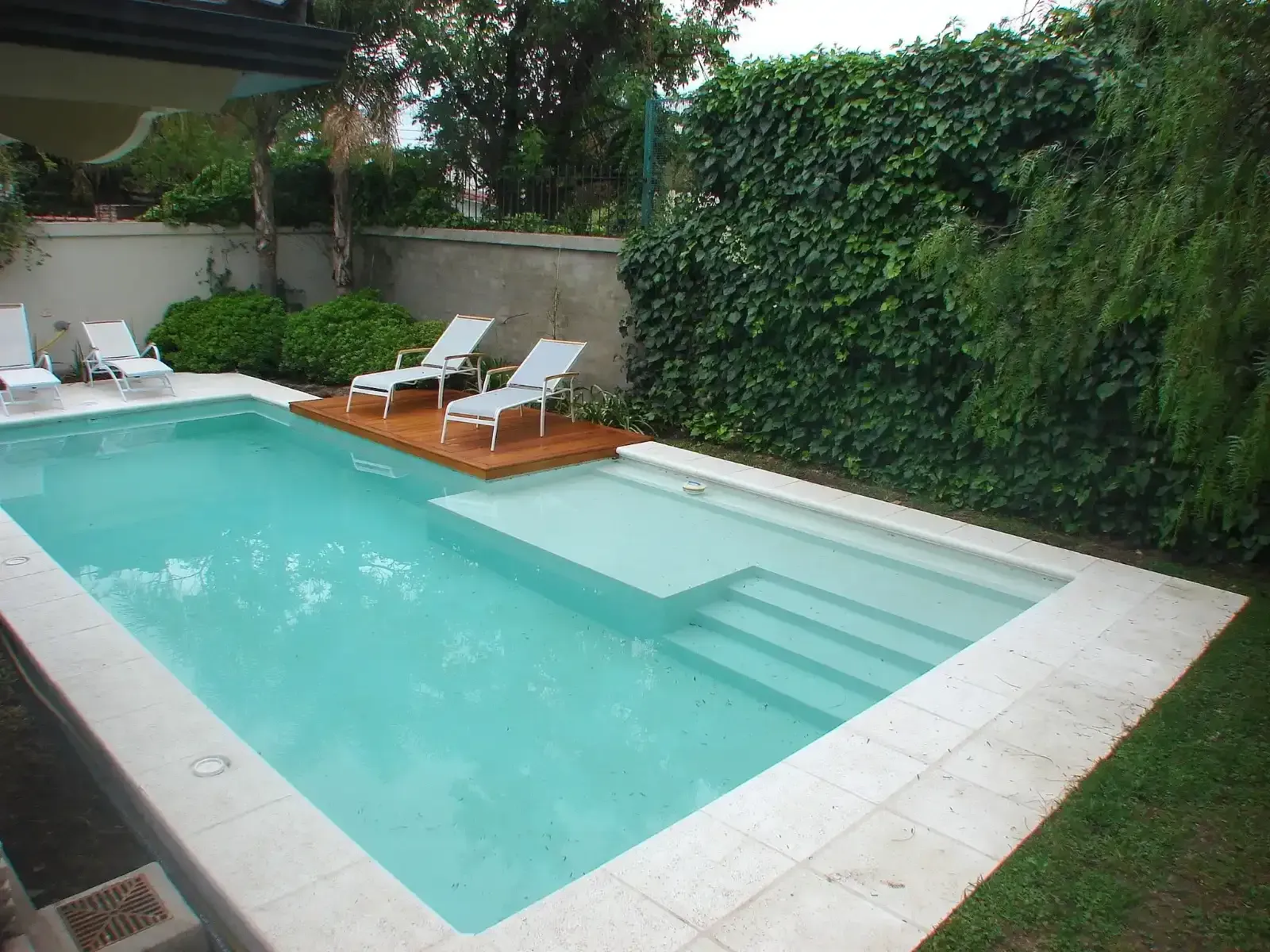 Una piscina rectangular de agua azul claro, una terraza de madera