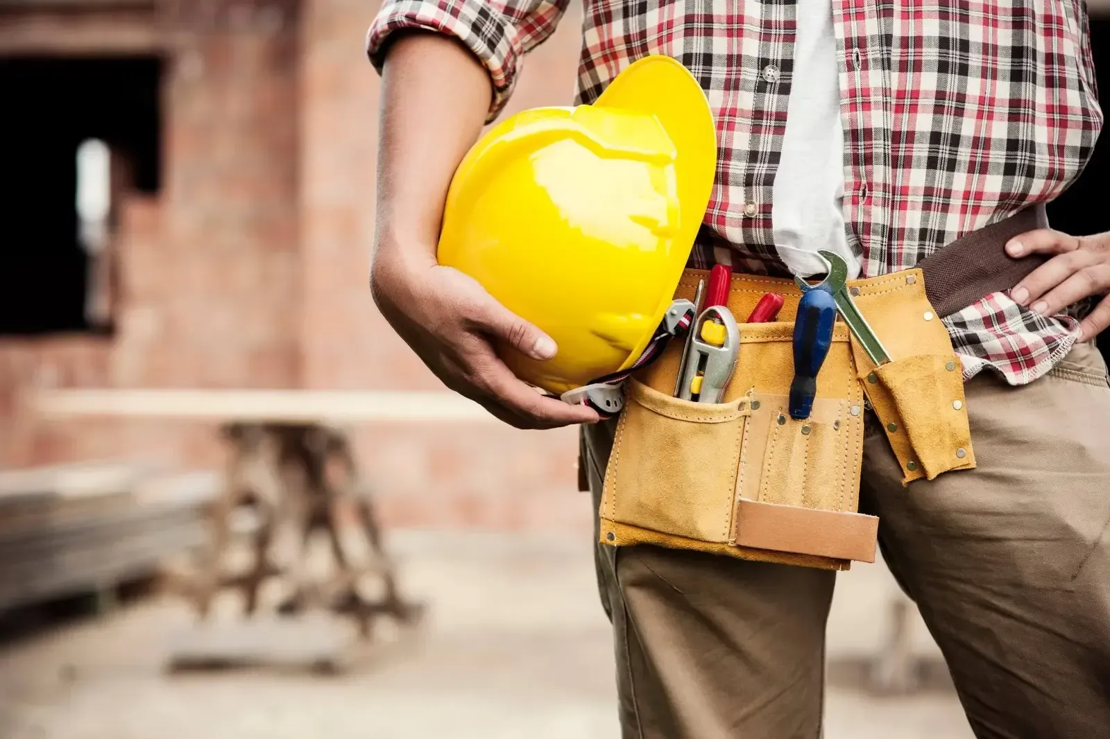 Un trabajador de la construcción con un casco amarillo y un cinturón de herramientas en una obra.