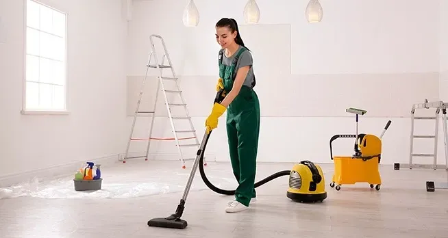 Una persona con un mono verde aspira una habitación limpia y moderna