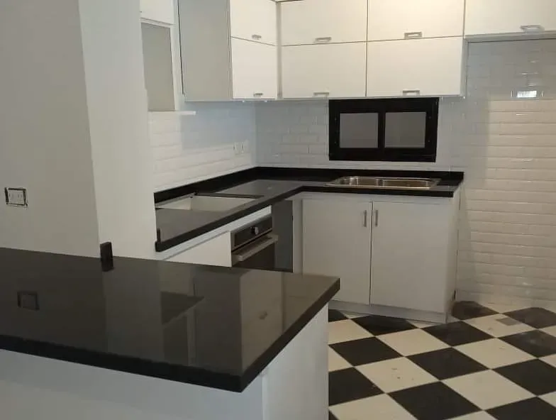 Una cocina moderna con armarios blancos, encimera negra y suelo de baldosas a cuadros blancas y negras.