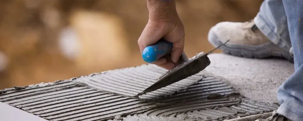 Una persona utiliza una llana dentada para extender mortero adhesivo sobre una superficie para la instalación de azulejos.