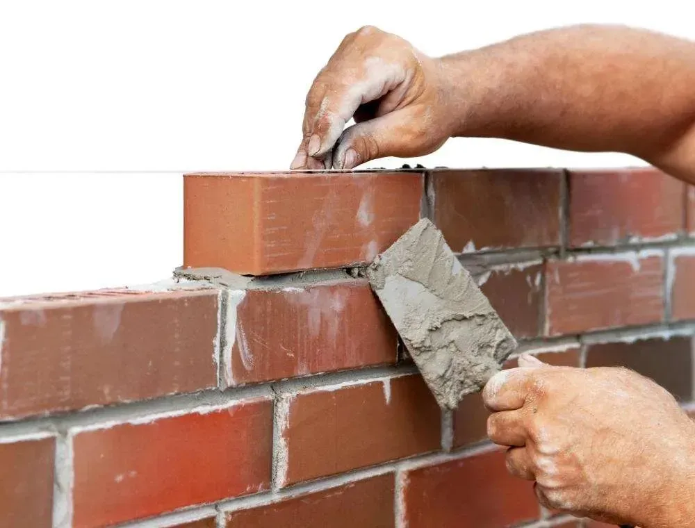 Primer plano de unas manos que utilizan una llana para aplicar mortero entre ladrillos rojos en una pared.