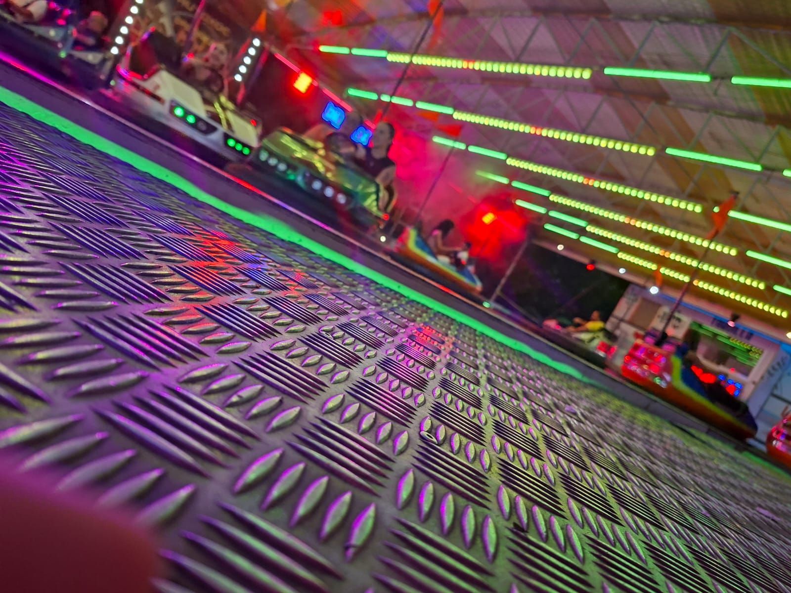 Autos chocadores en una pista iluminada y colorida. La gente los monta y conduce.