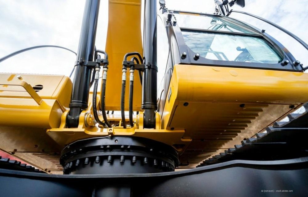 Gelber Baggerlöffel und Hydraulikarm heben Schutt an, von unten gesehen