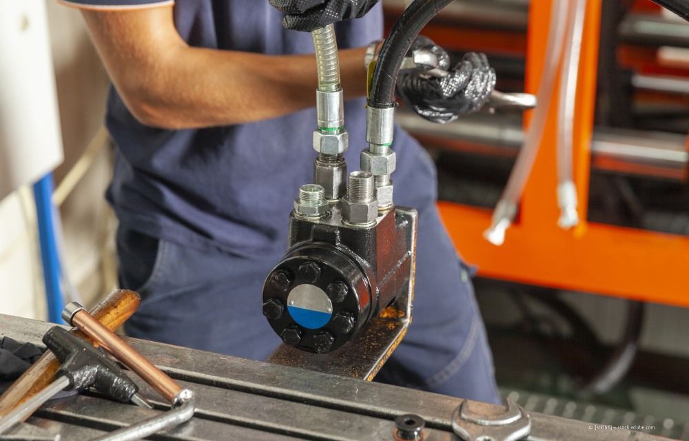 Ein Arbeiter bedient in einer Werkstatt ein Hydraulikwerkzeug an einem Metallteil.