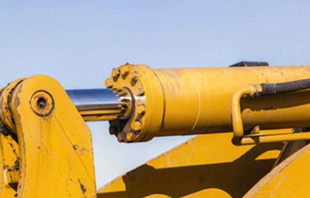 Gelber Hydraulikzylinder und Arm eines Baggers vor blauem Himmel
