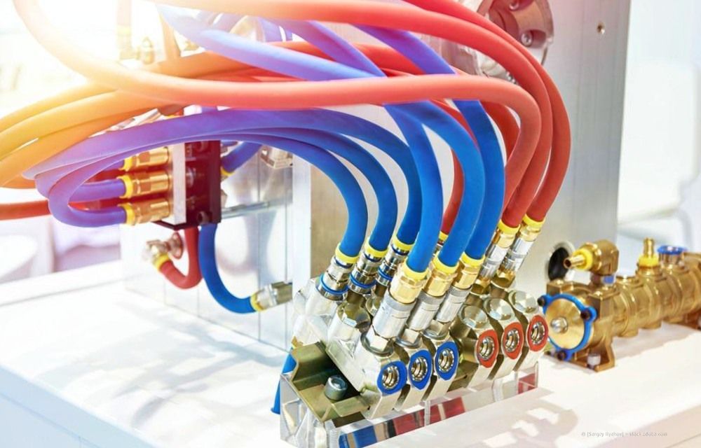 Bunte rote und blaue Schläuche sind in einer hellen Industrieumgebung an einen Messingverteiler angeschlossen.