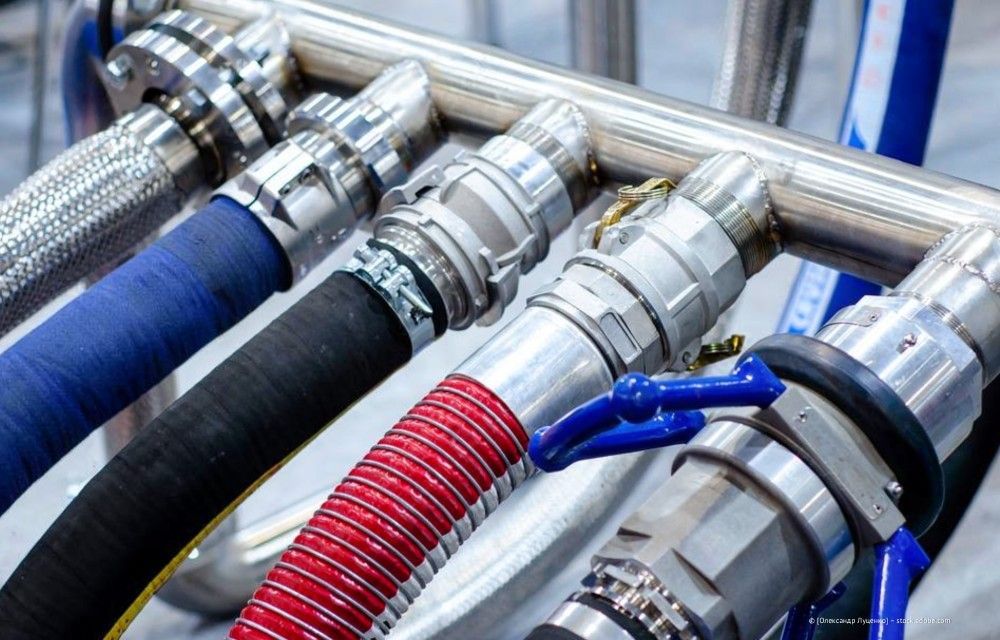 Nahaufnahme von Industrieschläuchen mit Metallkupplungen, die an einen Verteiler angeschlossen sind, darunter blaue und rote Schläuche.
