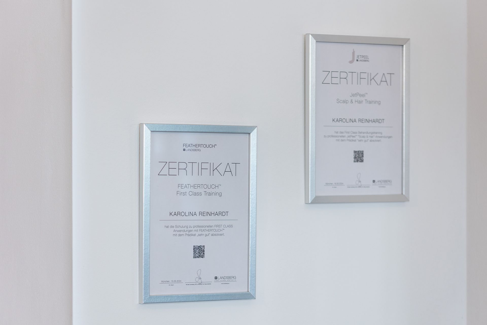 An einer weißen Wand hängen zwei Zertifikate.
