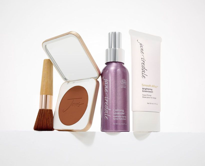 Eine Flasche Make-up von Jane Iredale und ein Pinsel auf einer weißen Oberfläche.