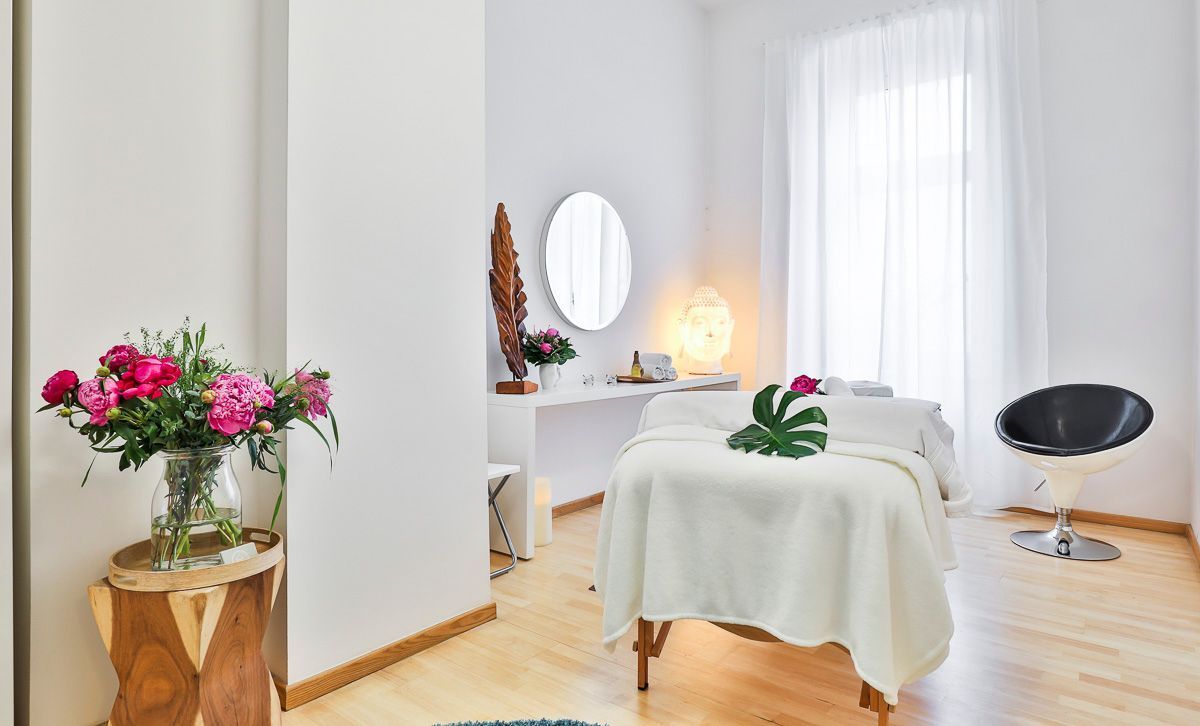 Ein Massagetisch in einem Raum mit einer Vase mit Blumen darauf.