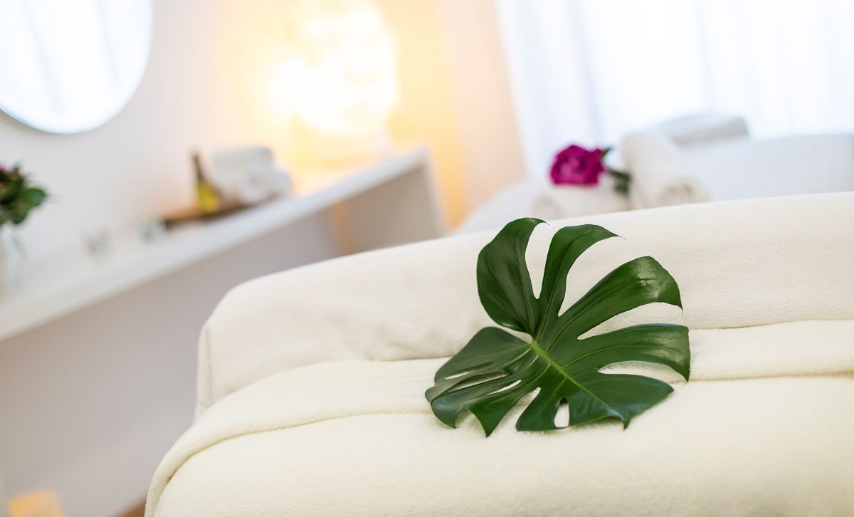 Ein grünes Blatt liegt auf einem weißen Handtuch auf einem Massagetisch.