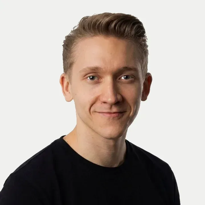 Hymyilevä henkilö mustassa paidassa vaaleaa taustaa vasten