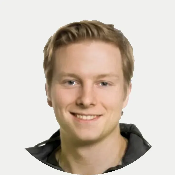 Hymyilevä lyhyet vaaleat hiukset omaava henkilö yksinkertaista valkoista taustaa vasten, yllään tumma kauluspaita.