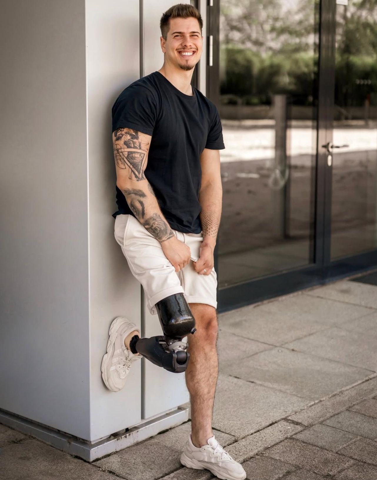 Junger Mann mit Tattoos und einer Beinprothese lehnt cool an einer Wand 