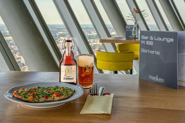 Ein Tisch in einer Bar mit Bier, Fladenbrot und Speisekarte, mit Blick auf die Stadt von einem hohen Gebäude aus.