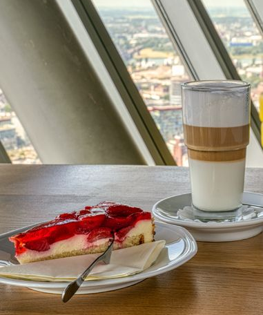 Erdbeer-Käsekuchen und geschichtetes Kaffeegetränk auf einem Tisch mit Stadtblick.
