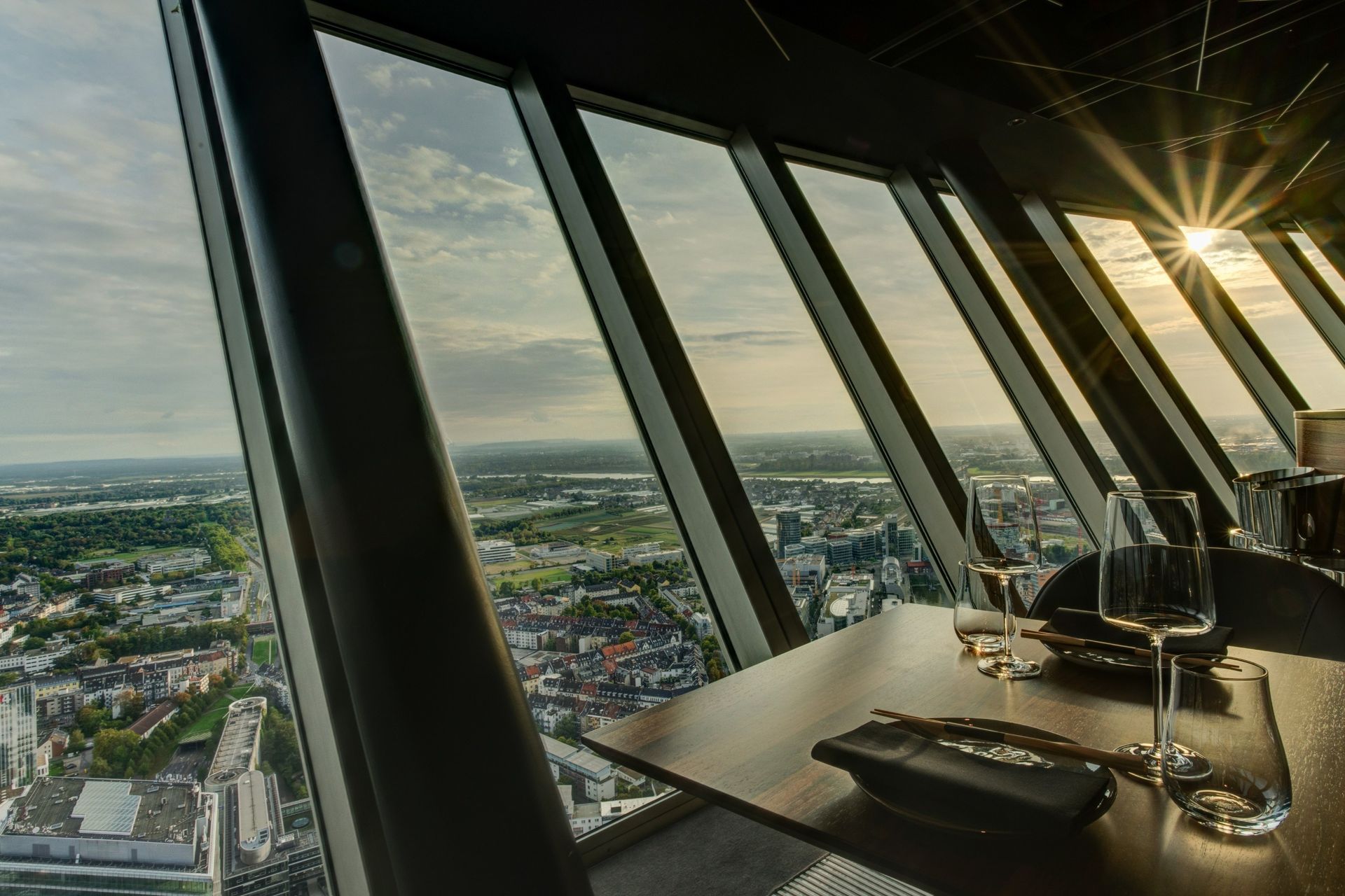 Ein Esstisch steht in der Nähe eines großen Fensters mit Blick auf die Stadtlandschaft bei Sonnenuntergang.