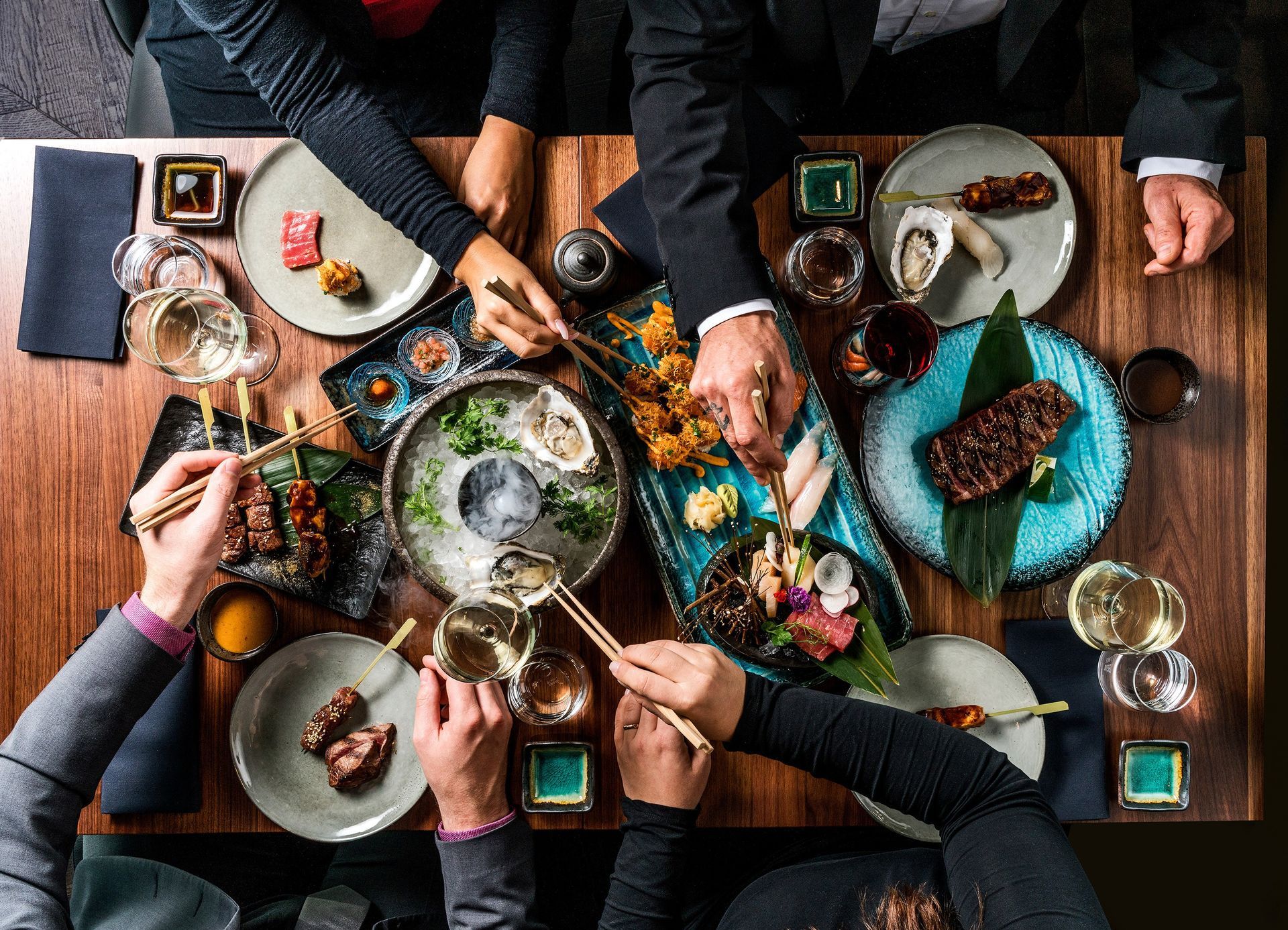 Menschen teilen sich an einem Holztisch mit Stäbchen verschiedene japanische Gerichte.