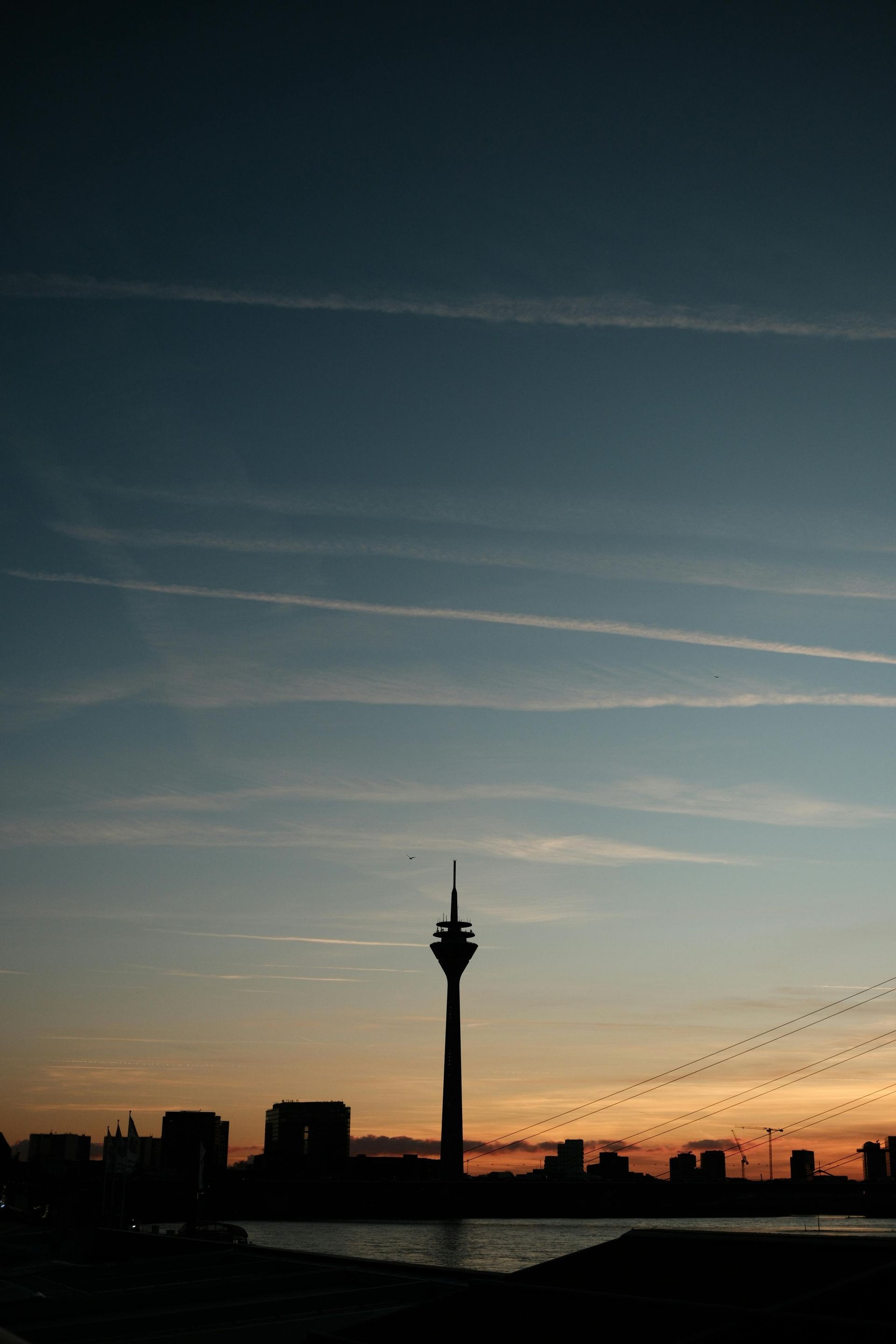 Silhouette des Rheinturms in Düsseldorf, Deutschland, bei Sonnenuntergang vor farbenprächtigem Himmel und Stadtkulisse.