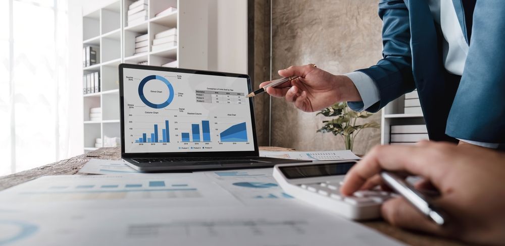 Profesionales de negocios revisando datos y gráficos financieros en la pantalla de una computadora portátil y una calculadora en una oficina.