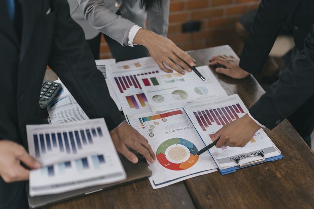 Profesionales de negocios analizan gráficos y datos en papeles extendidos sobre una mesa de madera.