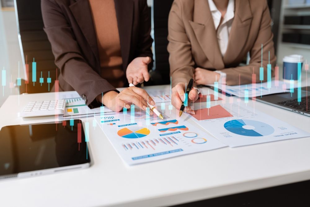 Dos profesionales analizan gráficos y datos financieros, con velas japonesas digitales superpuestas en su escritorio.