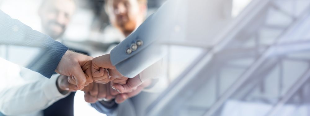 Dos personas vestidas de traje de negocios chocando los puños en un entorno de oficina.
