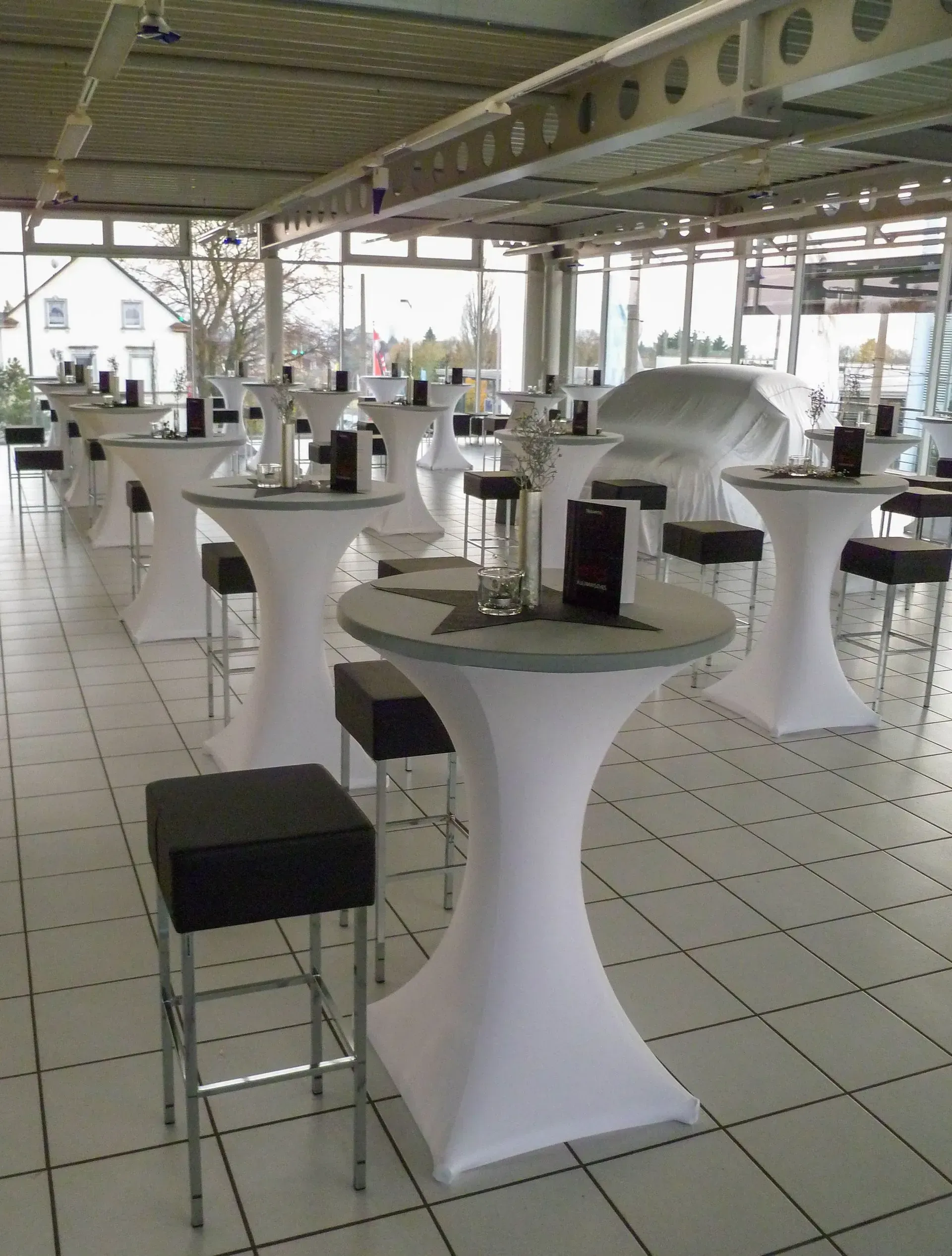 Eine Reihe weißer Tische mit schwarzen Hockern in einem Raum, Stefanie Cremerius raum-station