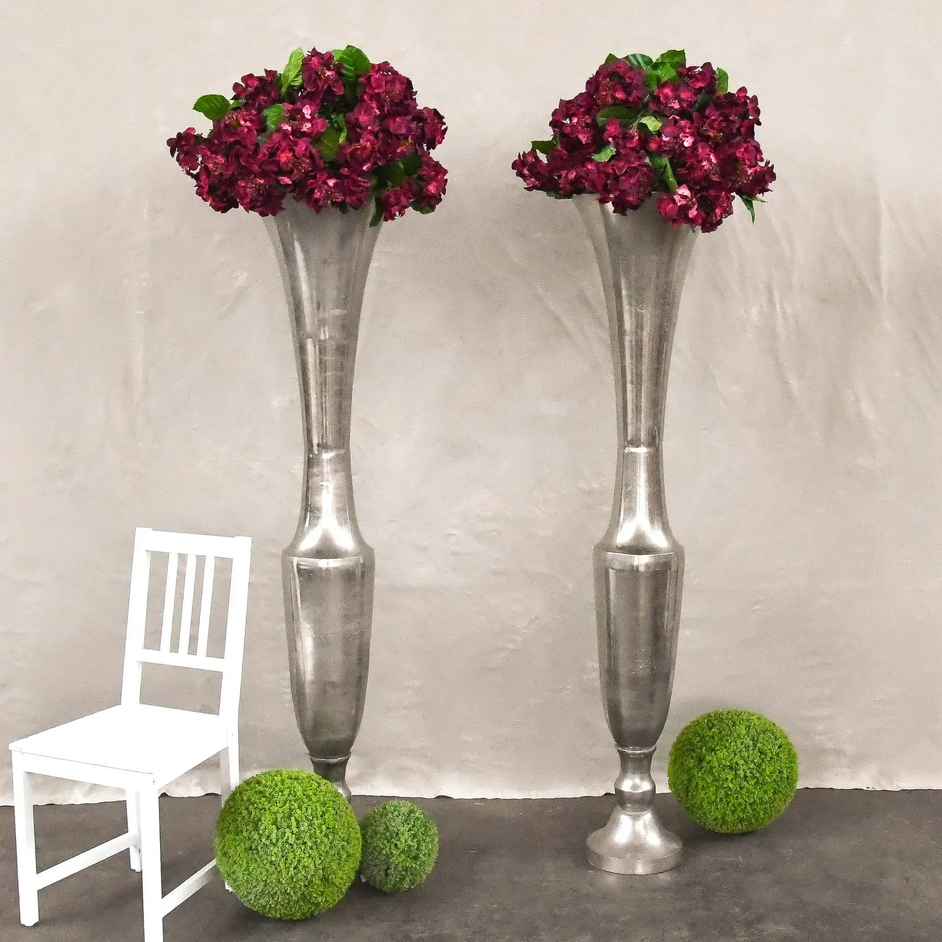Zwei silberne Vasen mit lila Blumen gefüllt neben einem weißen Stuhl, Stefanie Cremerius raum-station