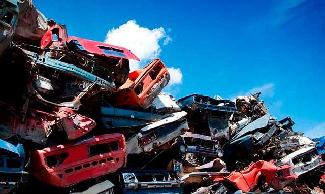 Una pila de coches destrozados contra un cielo azul con nubes.