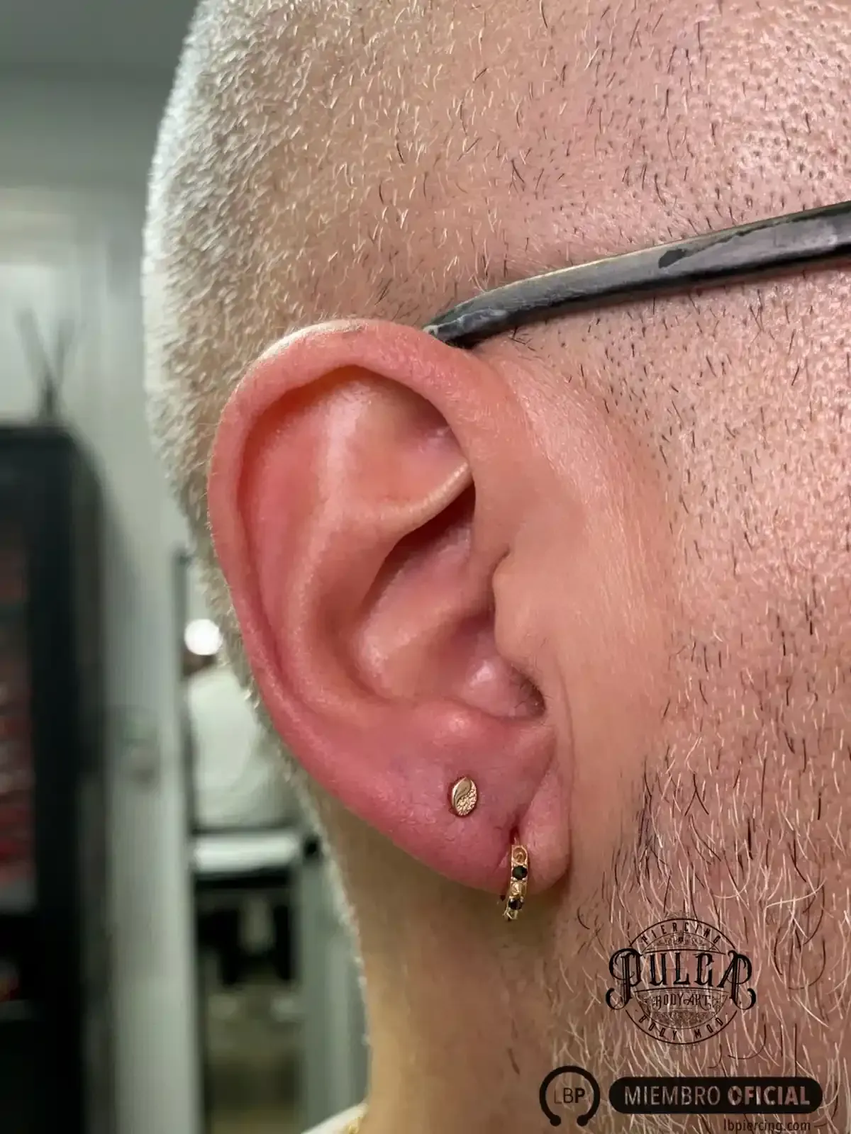 Primer plano de la oreja de una persona con dos pendientes: uno de botón y otro de aro. Piel clara.