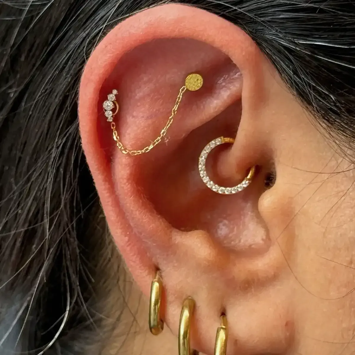 Oreja con múltiples piercings dorados: hélice, daith y dos aros en los lóbulos.