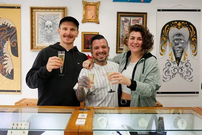 Tres personas en una joyería brindan con champán. Obras de arte cuelgan de las paredes.