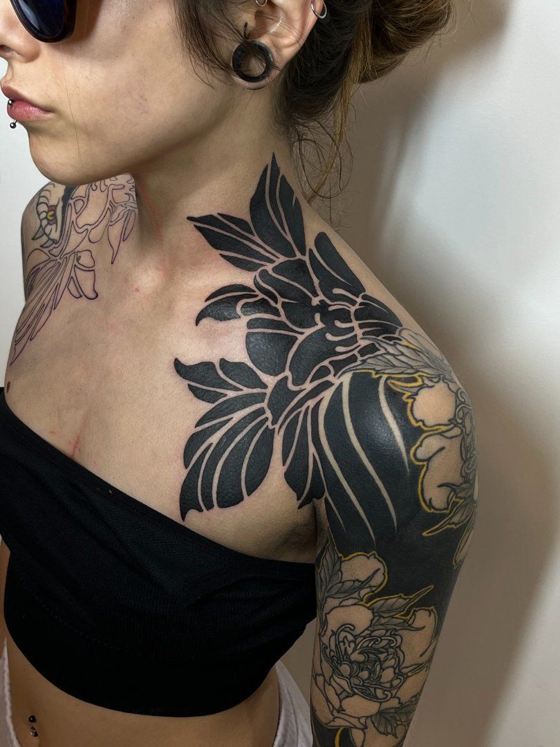 Mujer con tatuaje de flor negra en el hombro y el pecho, vistiendo un top tubo negro.